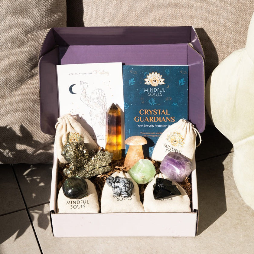 Mindful Souls crystal gift box featuring assorted healing stones, crystal guardians booklet, angel illustration card, and various crystals including amethyst, citrine, and black tourmaline arranged in an open purple box.